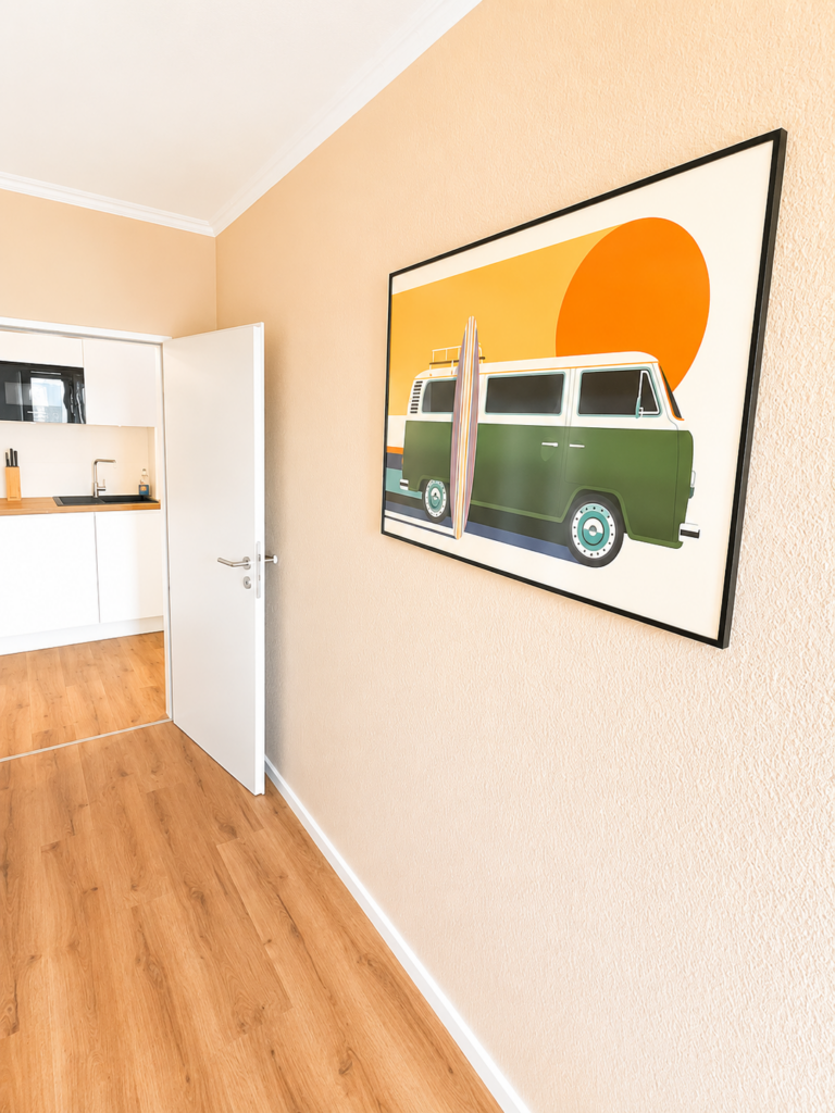Gerahmte Grafik eines grünen Campingbusses vor einer orangefarbenen Sonne im Kinderzimmer der ZweiteLiebe.
