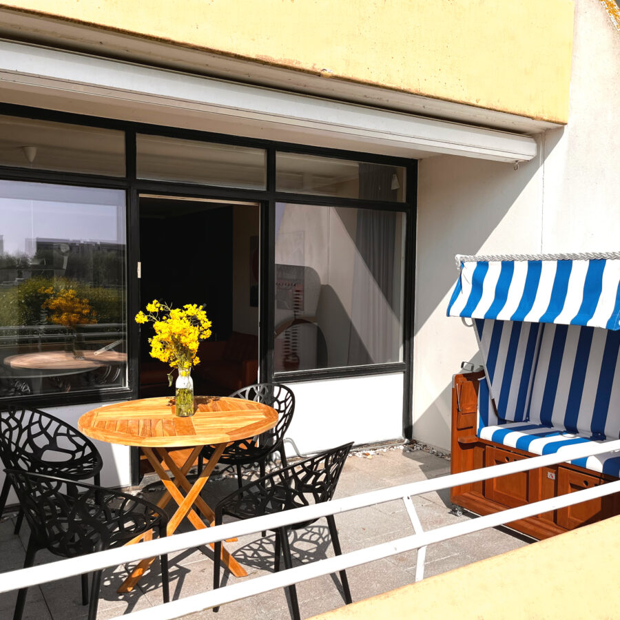 Seitlicher Blick auf die Terrasse der ZweiteLiebe mit Strandkorb, rundem Tisch und großer Fensterfront.