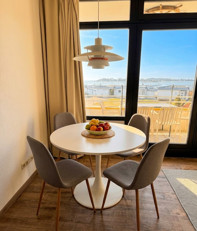 Runder Esstisch mit Obstschale und Pendelleuchte vor dem Balkonfenster der Meerzeitliebe mit Blick zum Yachthafen.