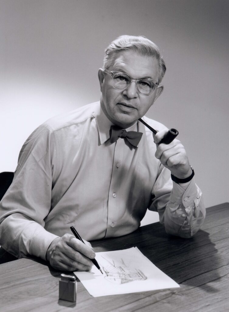 Arne Jacobsen am Schreibtisch, mit Brille, Fliege und Pfeife, über einer Skizze.
